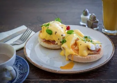 Eggs benedict on an English muffin with a cup of coffee beside it